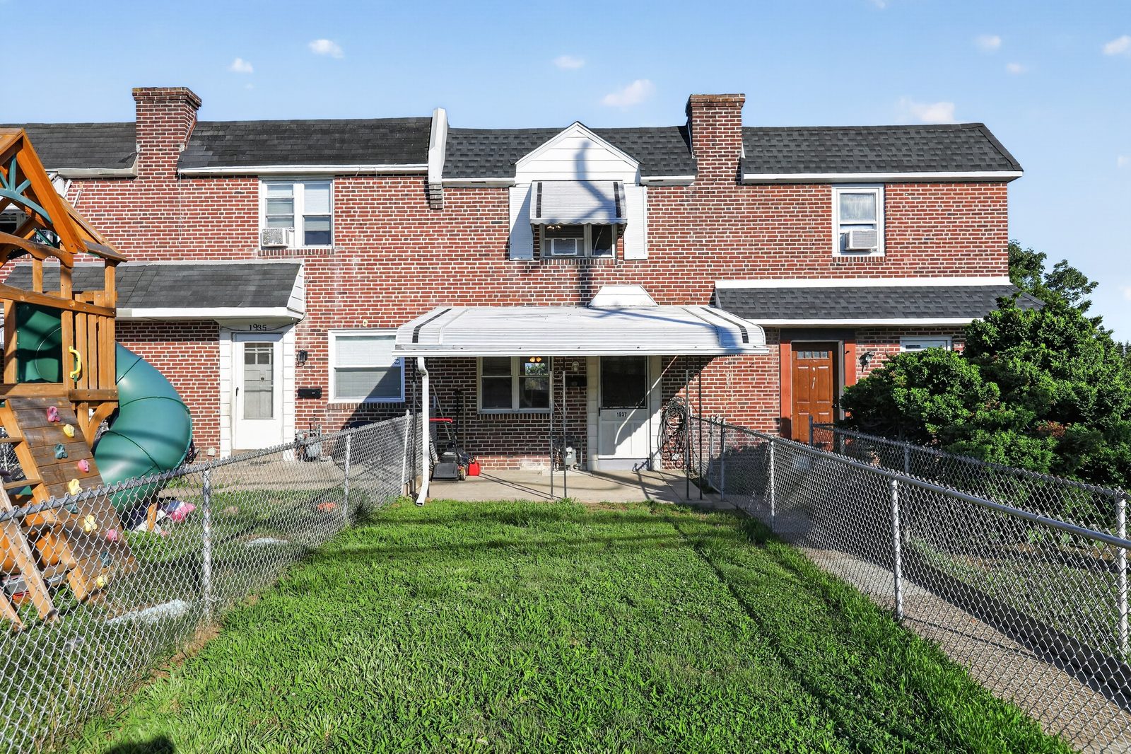 Front exterior of 1937 Delmar Dr — a refreshed brick townhouse with a covered front porch and fenced front lawn